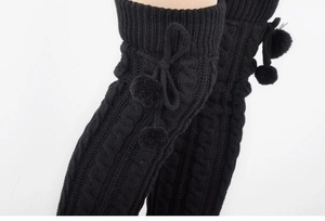 Detail of black cable-knit thigh high leg warmers with pom poms and bow decoration