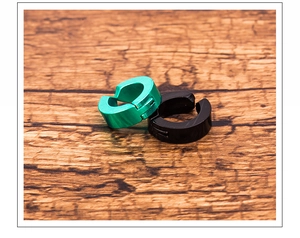 Macro shot of green and black C-shaped metal ear clips on a brown wooden texture