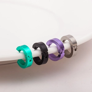 Four colors of stainless steel non-piercing ear clips on a white ceramic plate edge