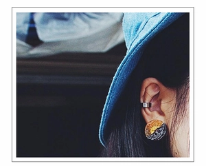 Close-up of textured round silver stud earring and sleek ear cuff on model ear