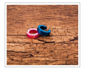 Blue and pink titanium steel ear cuffs displayed on a textured wooden surface