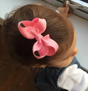 Pink grosgrain ribbon bow hair clip worn by a toddler in a natural indoor lifestyle setting