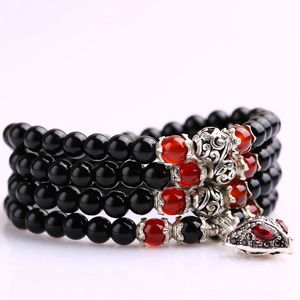 Detail of multilayer beaded bracelet with black beads and red glass accents and silver charms