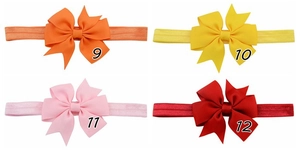 Detail of four baby bow headbands in orange, yellow, pink and red on elastic bands