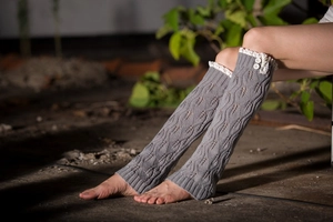Close-up of grey knitted leg warmers featuring white lace trim and decorative buttons