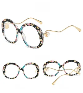 Detail view of oval floral frame sunglasses with golden wavy temples and pearl accents