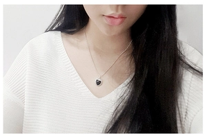 Detail of a minimalist S925 silver necklace with a black heart pendant worn on a model