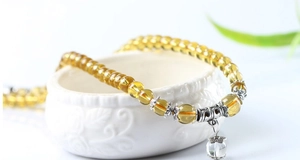 Yellow crystal beaded bracelet with silver charm displayed on a white ceramic bowl