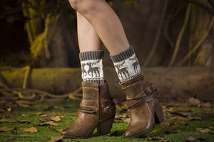 Close-up of moose pattern knitted boot cuffs with brown leather boots on forest leaves