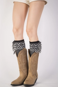 Close-up of knit leg warmers with bohemian geometric patterns and fringe over cowboy boots