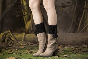 Detail view of black knit leg warmers with fringes paired with stylish beige leather boots