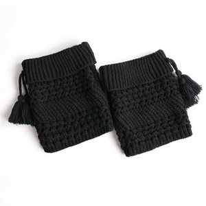Close-up of black knitted leg warmers with textured acrylic yarn and fringe details