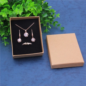 Rose gold jewelry set with white stones in kraft paper gift box on blue background