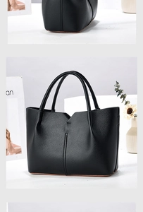 Detail of black pebbled leather tote bag featuring unique V-shaped opening and orange trim