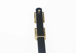 Détail de ceinture en cuir verni noir avec boucle rectangulaire dorée et rivet de fixation