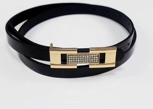 Détail d'une fine ceinture en cuir verni noir avec boucle dorée ornée de strass brillants