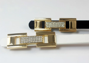 Détail de fines ceintures en cuir verni avec boucles strass dorées en noir et blanc