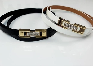 Détail de ceintures fines noires et blanches avec boucles dorées ornées de strass brillants