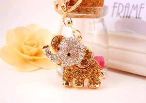 Close-up of golden elephant keychain with sparkling rhinestones on a warm pink background