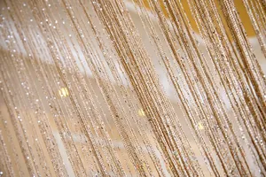 Macro detail of high-density champagne gold tassel curtain with sparkling metallic threads