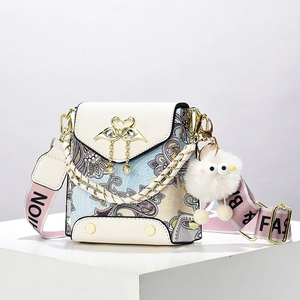 Fashionable paisley crossbody bag with leather flap and pink lettered strap on white stand