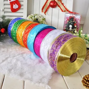 Nine colorful rolls of Christmas glitter ribbons with gold swirl patterns on white wood background