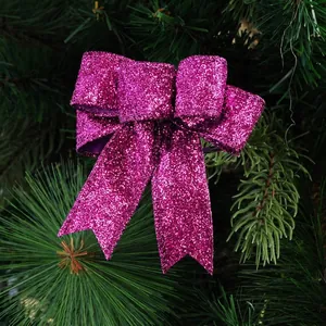 Sparkling purple glitter Christmas bow ornament hanging on a lush green pine branch