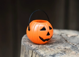 Close-up of a small orange Halloween pumpkin candy bucket on a rustic wood stump