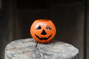 Close-up of an orange plastic Halloween pumpkin bucket placed on a rustic wood stump