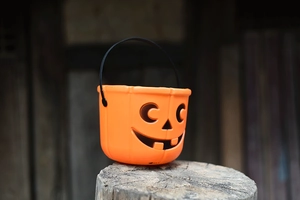 Close-up of an orange Halloween pumpkin candy bucket with black handle on a wood log