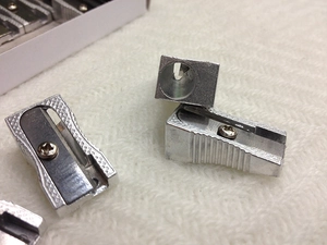 Macro detail of silver aluminum single-hole pencil sharpener showing metal texture
