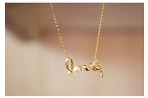 Detailed close-up of golden Love pendant necklace with a white pearl and sparkling crystal