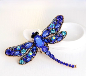 Detailed close-up of a vintage dragonfly brooch with blue crystals on a ceramic surface