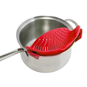 Close-up of a red silicone clip-on pot strainer attached to a stainless steel stockpot edge