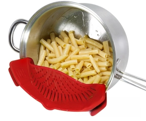Red silicone clip-on pot strainer filtering pasta from a stainless steel pot
