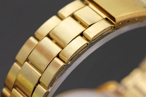 Macro shot of gold-plated metal watch strap detailing fine brushed and polished textures