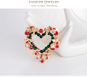 Detail view of a heart-shaped Christmas wreath brooch with colorful rhinestones on a white hand mold