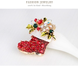 Detail of a Christmas boot brooch featuring red rhinestones and green enamel leaf design