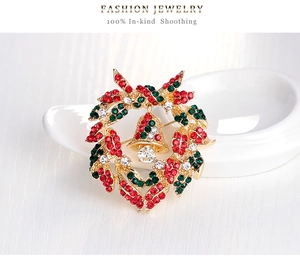 Close-up of golden Christmas wreath brooch with red and green rhinestones and a bell