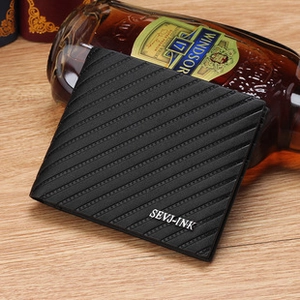Détail d'un portefeuille noir en cuir strié avec logo métallique sur une surface en bois