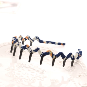 Detail of a wavy headband with blue, white, and orange fabric and black inner teeth