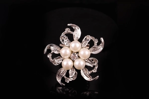 Vista macro della spilla a fiore argentata con perle bianche e strass su sfondo nero