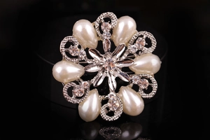 Dettaglio della spilla a ghirlanda argentata con perle e cristalli su superficie riflettente