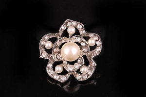 Dettaglio spilla a fiore argento con grande perla e cristalli su sfondo nero di lusso