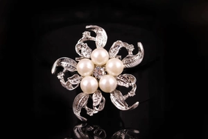 Dettaglio macro di una spilla floreale in argento con perle lucenti e accenti di cristallo