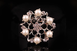 Primo piano di una spilla floreale in argento con perle e strass su sfondo nero