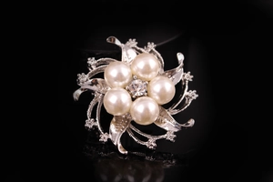 Dettaglio di una spilla a fiore in argento con cristalli e perle su sfondo nero professionale