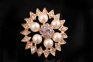 Macro di una spilla dorata con strass di cristallo e sei eleganti perle bianche