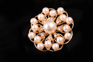 Dettaglio di una spilla floreale dorata con perle bianche e cristalli brillanti