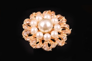 Macro di una spilla floreale dorata con perla centrale e petali di strass